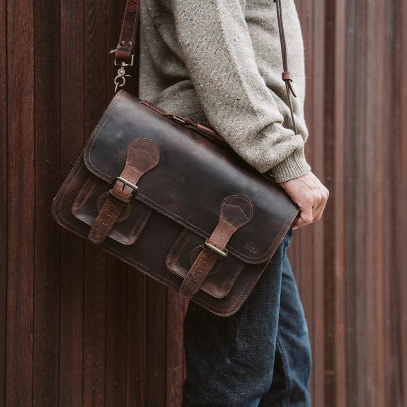 Man holding a dark oak Roosevelt leather briefcase with antique brass buckles and adjustable shoulder strap.
