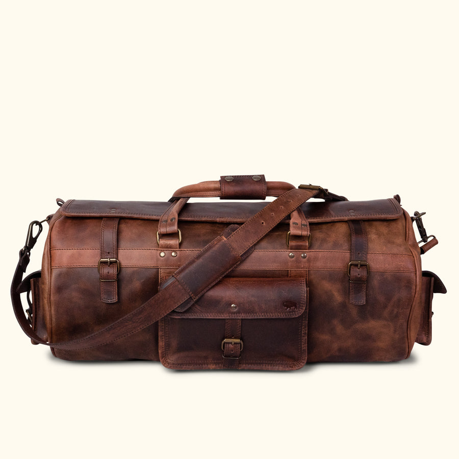 Dark oak buffalo leather duffle bag with adjustable shoulder strap, top handles, and secure buckle closures for travel.