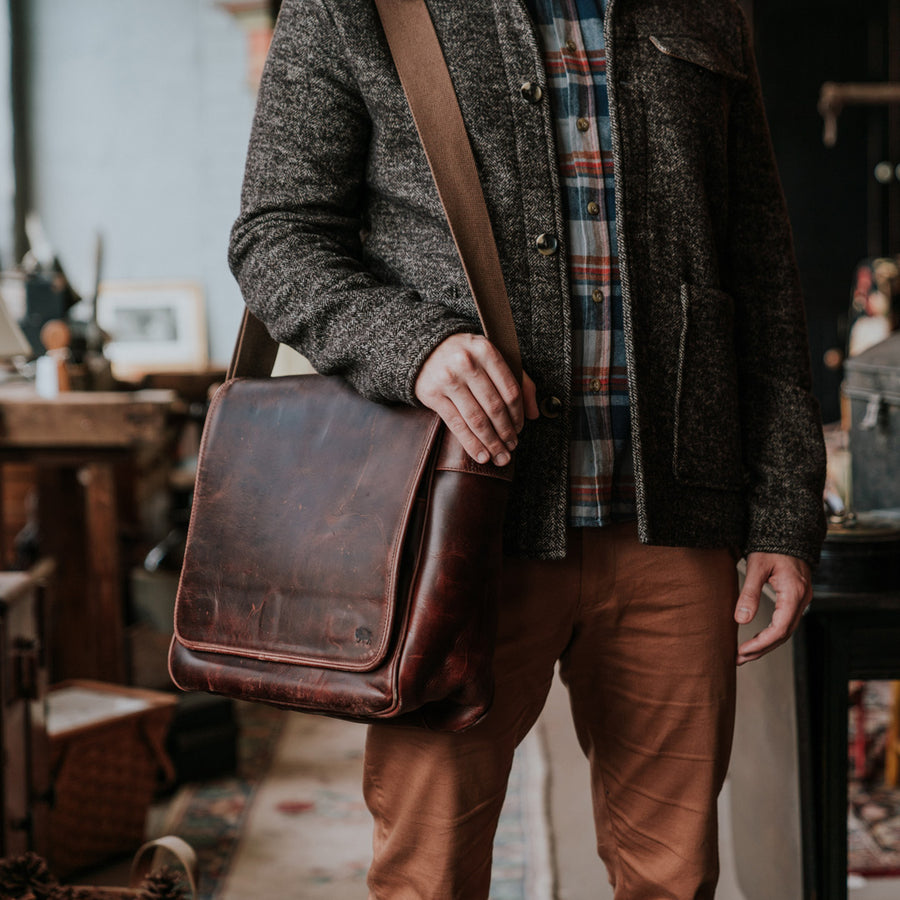 Elegant dark oak brown leather satchel with a wide, adjustable canvas strap, showcasing a smooth, well-worn patina and classic design.